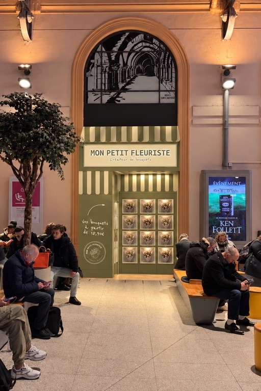 Le distributeur Mon Petit Fleuriste, avec son store rayé et son enseigne, installé sous une arche de la gare Saint-Lazare